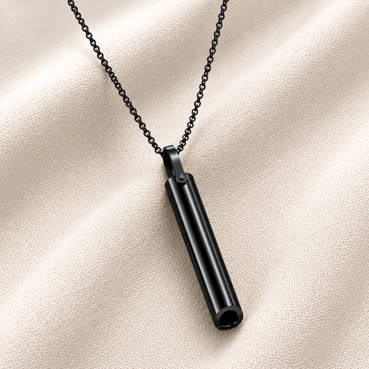 A black breathing necklace on a matching black chain, displayed on a textured beige fabric background.