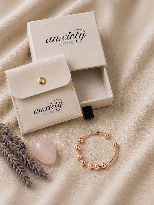 A rose gold beaded open-bend fidget ring displayed next to its cream-colored branded storage pouch and matching box on a beige fabric background.