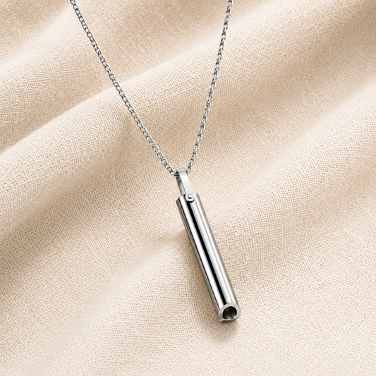 A silver breathing necklace on a delicate chain, displayed against a textured beige fabric background.