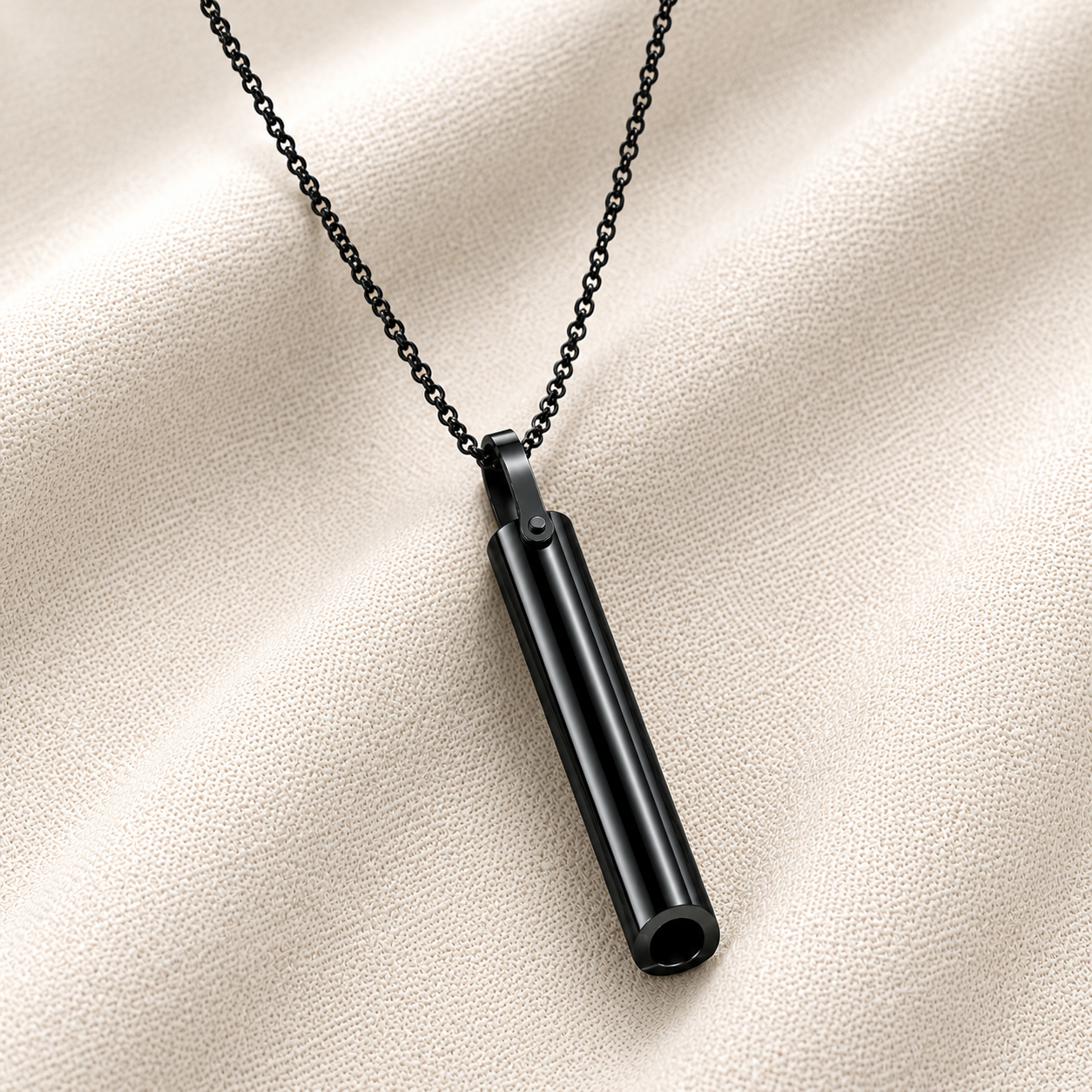 A black breathing necklace on a matching black chain, displayed on a textured beige fabric background.