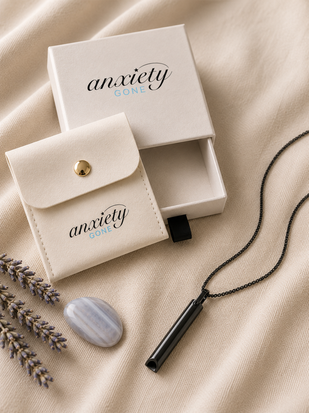 Anxiety Gone black breathing necklace with a black chain, displayed next to its cream-colored presentation box and matching pouch on a beige fabric background.