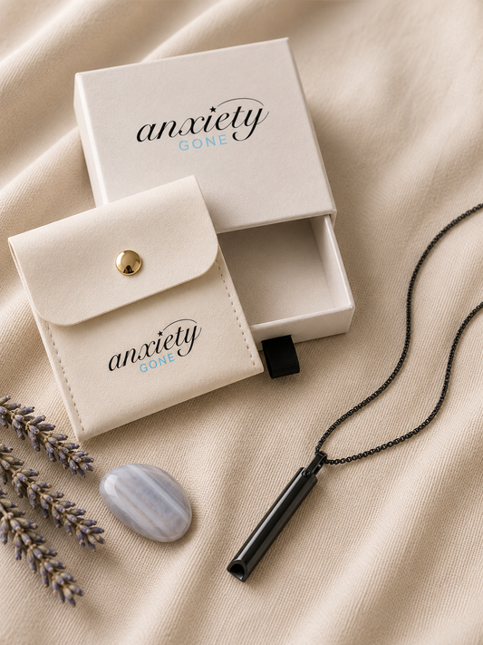 Anxiety Gone black breathing necklace with a black chain, displayed next to its cream-colored presentation box and matching pouch on a beige fabric background.