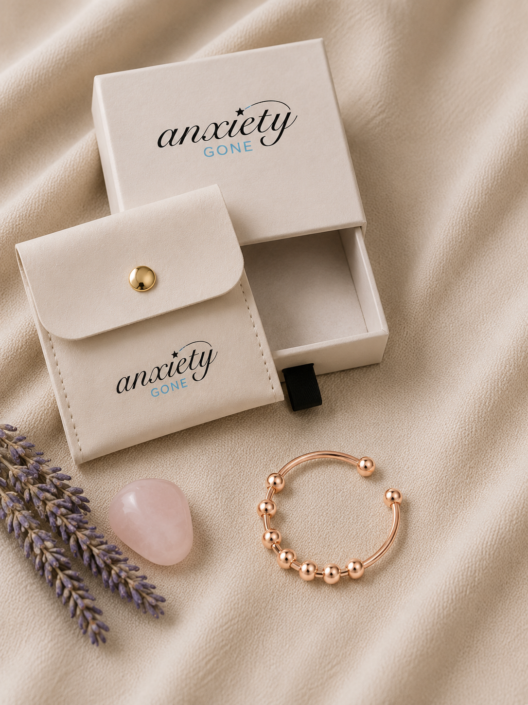 A rose gold beaded open-bend fidget ring displayed next to its cream-colored branded storage pouch and matching box on a beige fabric background.