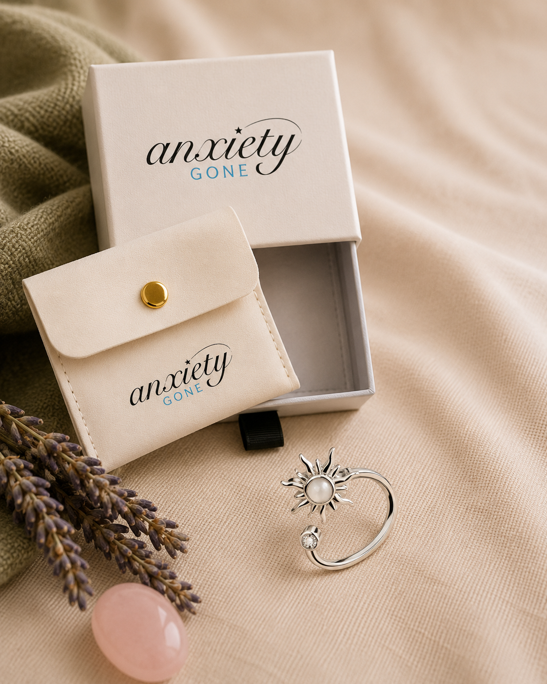 Anxiety Gone brand jewelry box set with a silver sunburst fidget ring on a beige fabric background with decorative lavender and a pink stone.