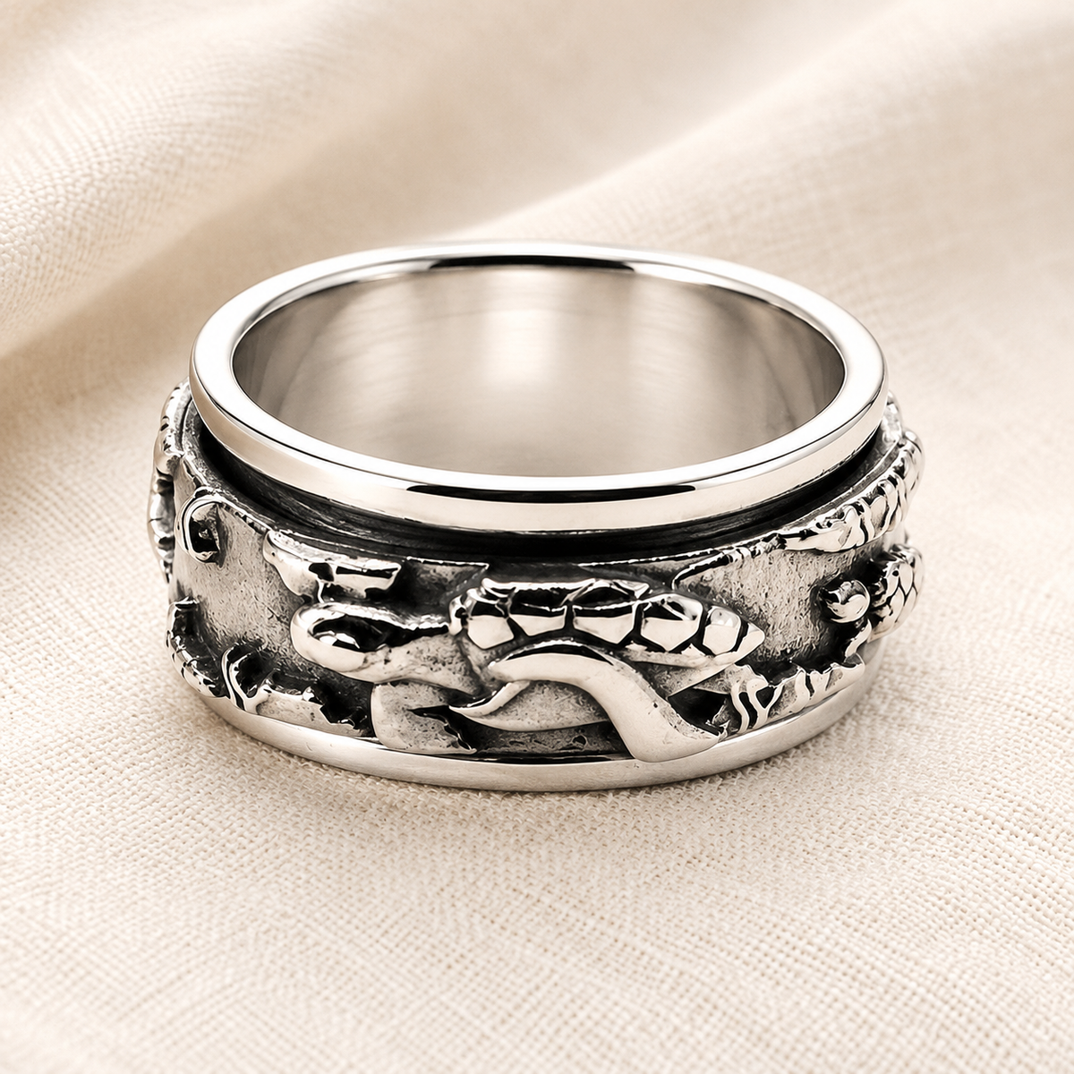 A sterling silver spinner ring with a detailed turtle design, resting on a textured beige fabric background.