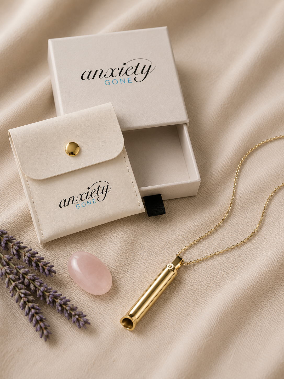 Gold breathing necklace on a delicate chain, displayed with its white branded jewelry box and small white pouch on a soft beige fabric background, alongside a pink stone and lavender sprigs.
