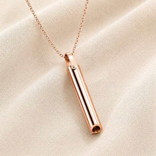 A rose gold breathing necklace on a delicate chain, displayed on a textured beige fabric background.