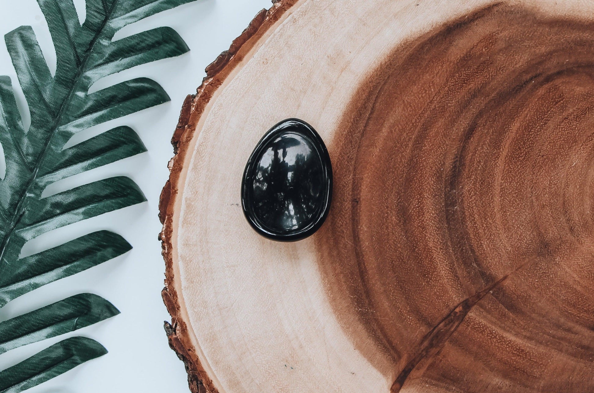Polished black obsidian worry stone with mirror-like sheen and thumb indentation